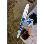 A top-down view of a woman adjusting her Women's Aspect ski on a wooden dock, with a Connelly life vest nearby.