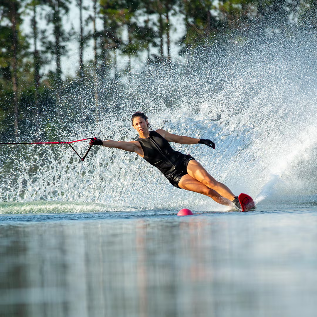 Person waterskiing on a lake, creating a large spray, with trees in the background.
