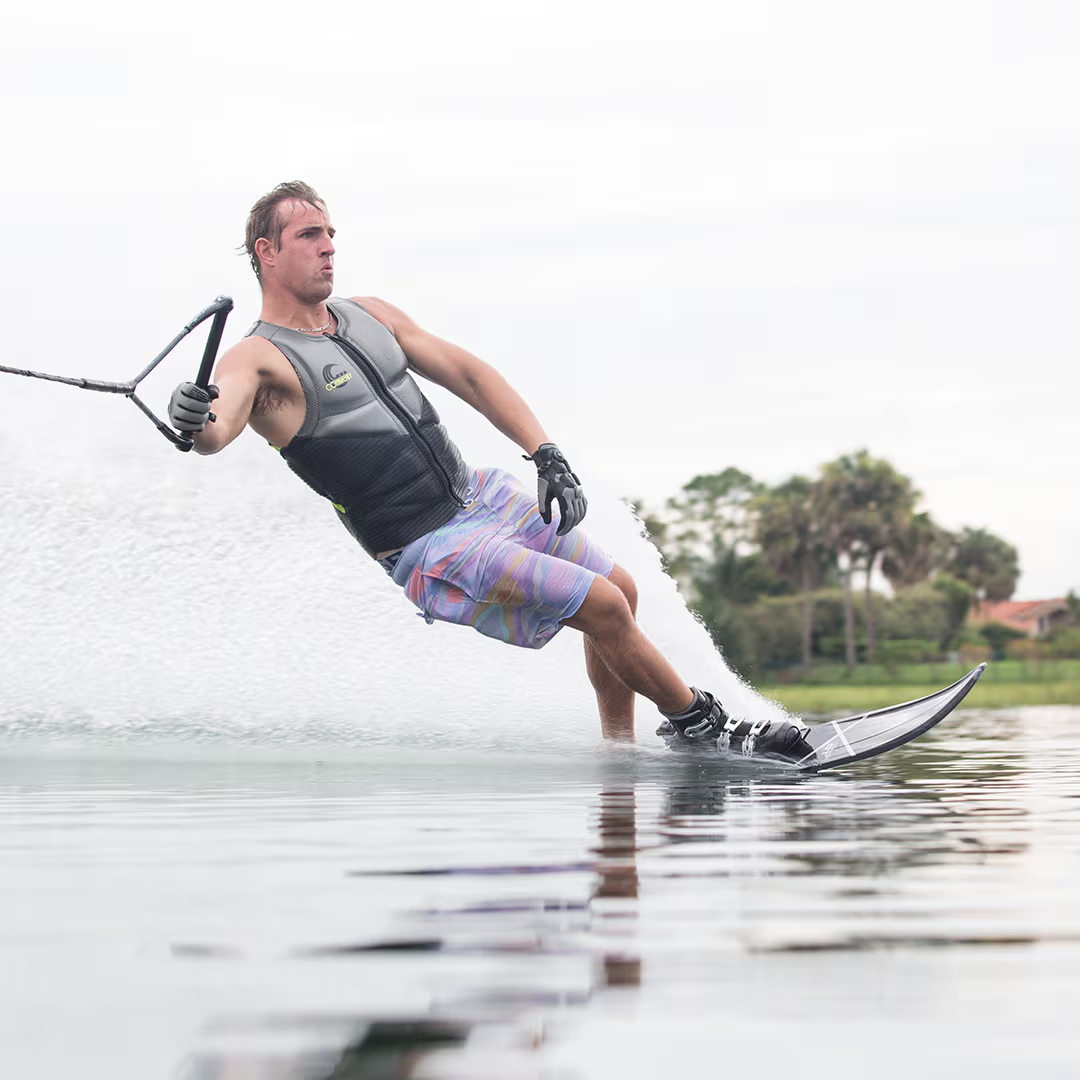 Person waterskiing on a lake, wearing a vest and gloves, creating a splash.