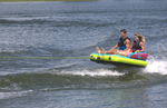 Two riders sitting upright, gliding across the water on the Fun 2, a bright blue and yellow inflatable towable tube.