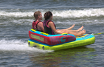 Rear view of the Fun 2 towable tube with two riders leaning back, gripping handles, and speeding across the water.
