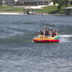 Fun 3 towable tube with three riders sitting upright, holding handles, and gliding across the water on a bright inflatable.