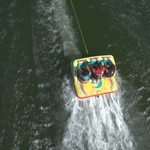 Fun 3 towable tube with three riders gripping handles as they are pulled across the water, leaving a wake behind them.
