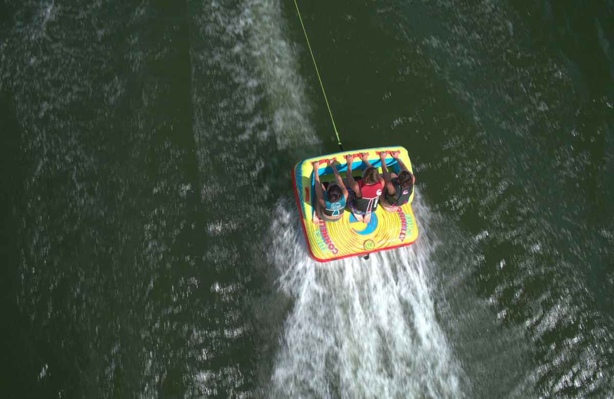 Fun 3 towable tube with three riders gripping handles as they are pulled across the water, leaving a wake behind them.