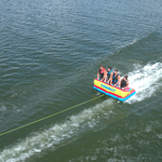 Fun 4 towable tube with four riders, a visible wake trail, and a tow rope extending forward.