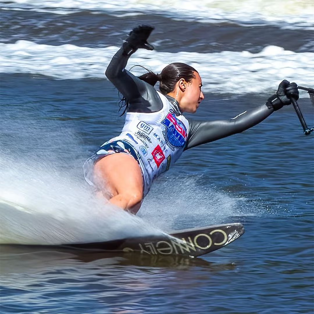 Person water skiing, leaning sharply, creating a spray on a sunny day.