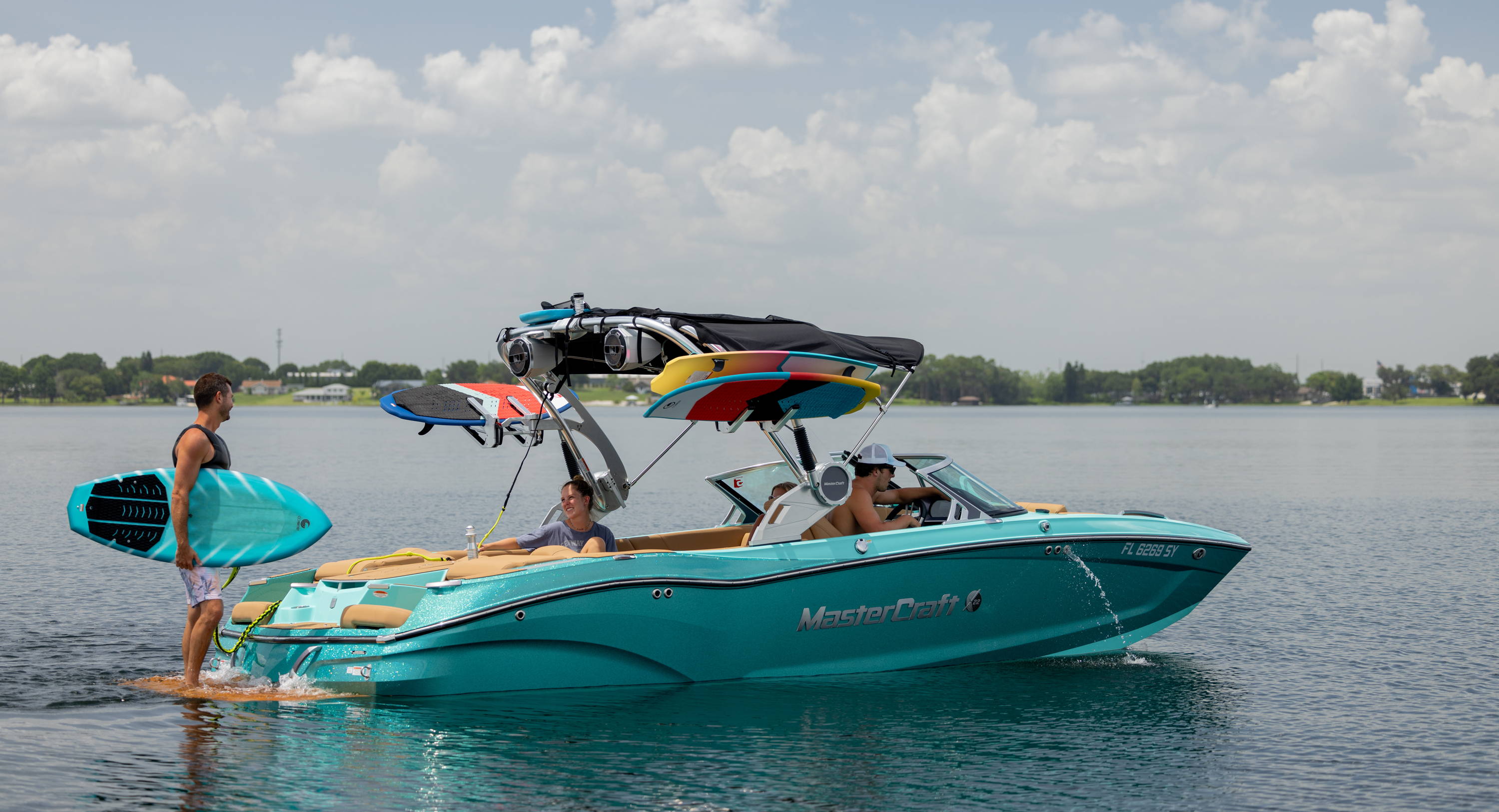 People with surfboards on a turquoise motorboat in a calm lake.