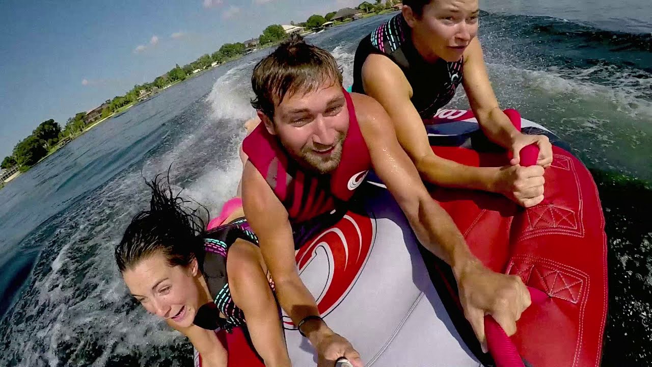 Three people joyfully riding an inflatable tube on the water.