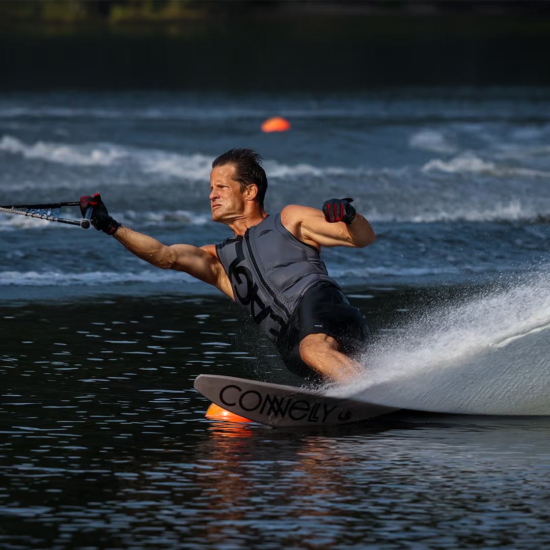 Person waterskiing sharply on a lake, creating a splash, wearing a gray life vest.