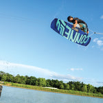 The 2024 Groove wakeboard in mid-air, showcasing its bold blue and teal graphics with dynamic water spray.