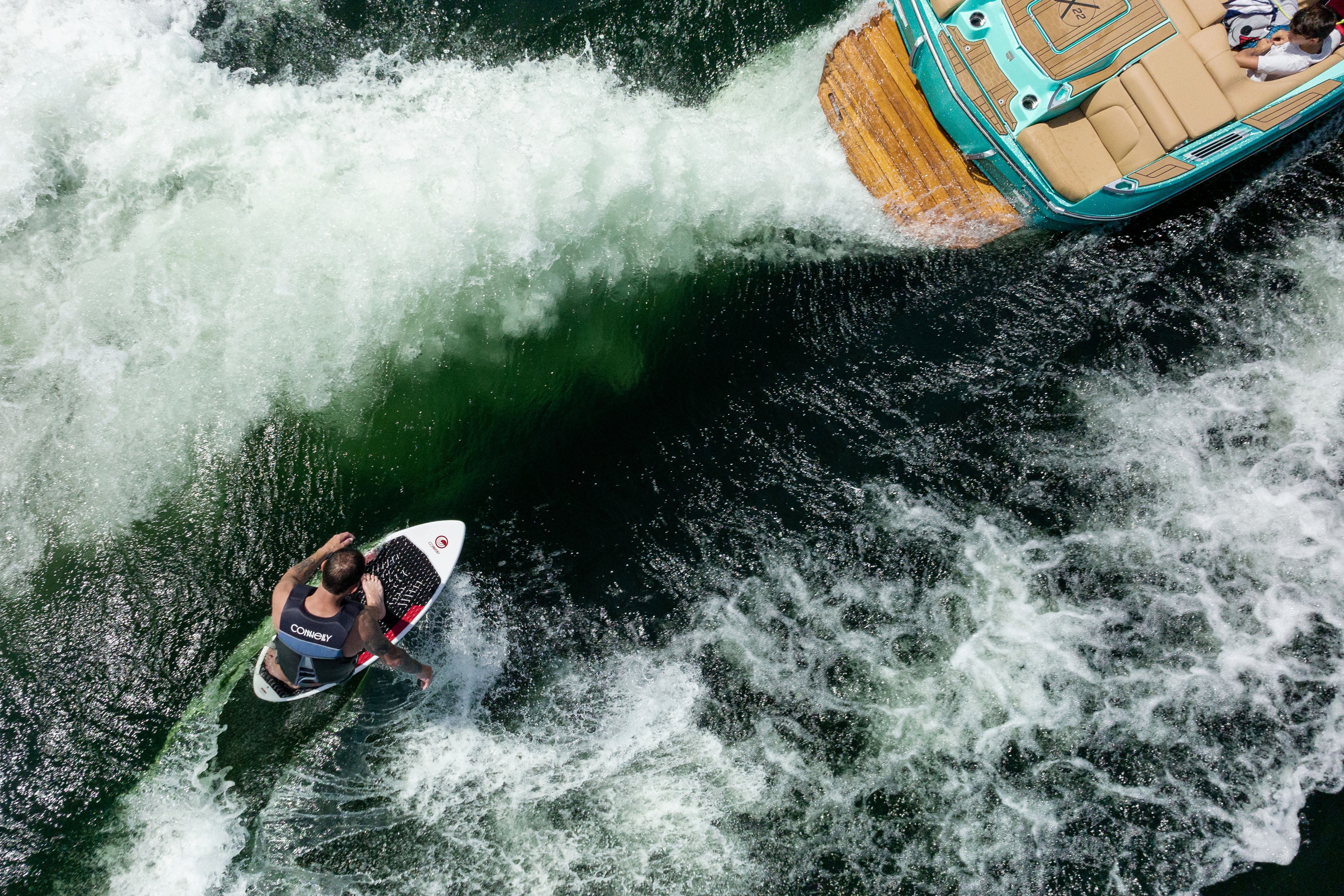 Person wakeboarding beside a boat, creating waves on a greenish body of water.