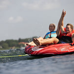 Two riders in life jackets enjoying the Racer 2 towable tube, speeding over the water with splashes around them.