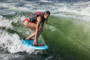 A rider in a red swimsuit surfing on the Stratus board, balancing on a wave with a focused stance.