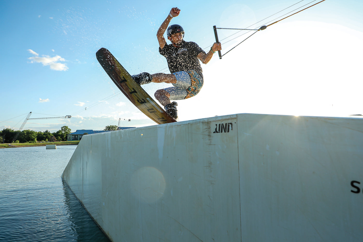 On a sunny day, a wakeboarder jumps off a ramp with the 2024 Woodros buttery smooth flex.