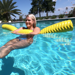 Woman relaxing in a pool with a yellow Mega Party Noodle, holding the floating noodle while enjoying a sunny day.