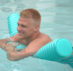 Man in a pool leaning on a mint Deluxe Party Noodle with a textured, ridged design, smiling and relaxed.