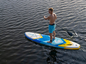 Man paddling the Tahoe ISUP on the water, wearing blue shorts and a waist leash.