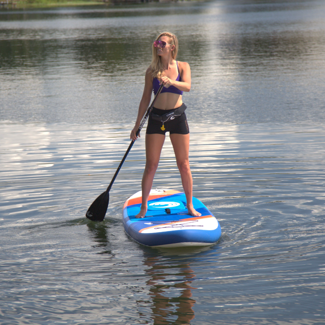 A woman stands and paddles on the Pacific ISUP, wearing a purple sports bra and black shorts.