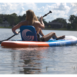 A woman paddles on the Pacific ISUP in a seated position, using the attached backrest for support.