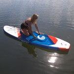 A woman kneels on the Pacific ISUP, adjusting the built-in storage hatch.